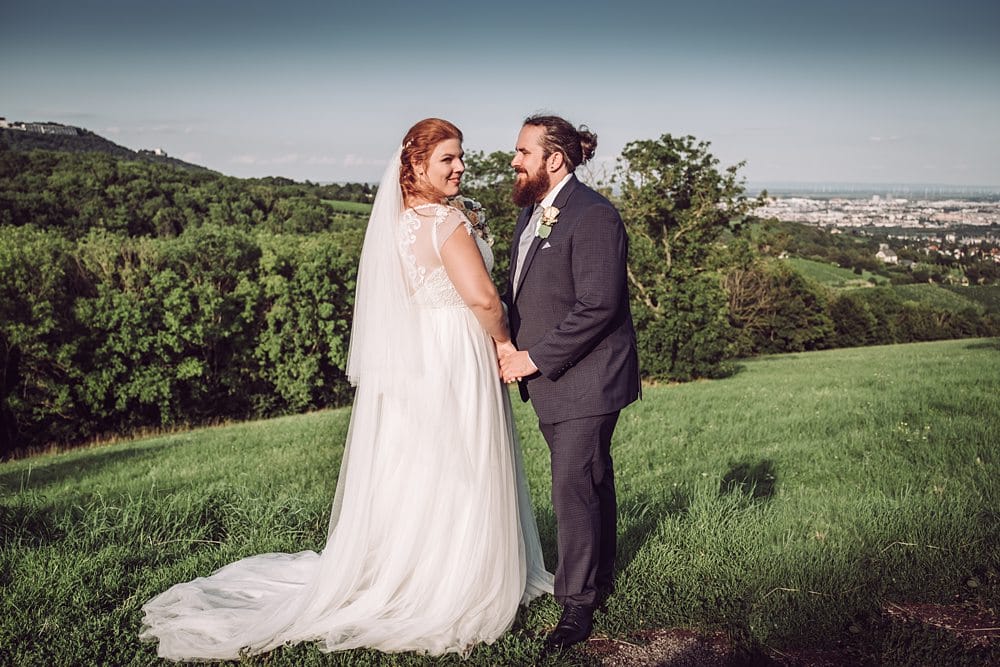 Eine Braut und ein Bräutigam stehen auf einem grasbewachsenen Hügel.