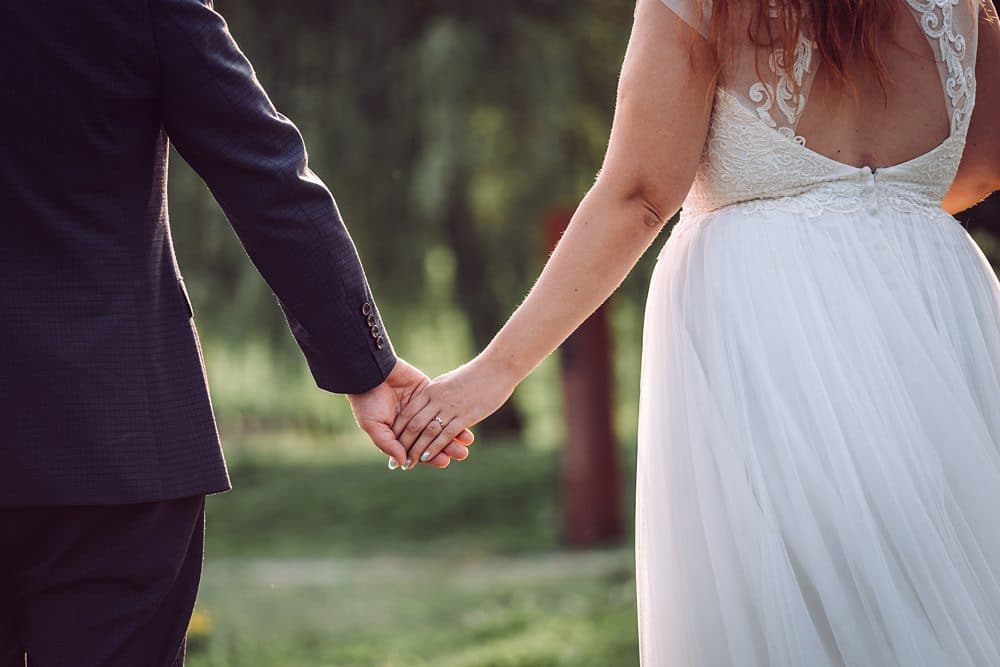 Eine Braut und ein Bräutigam halten sich an den Händen auf einem Feld.