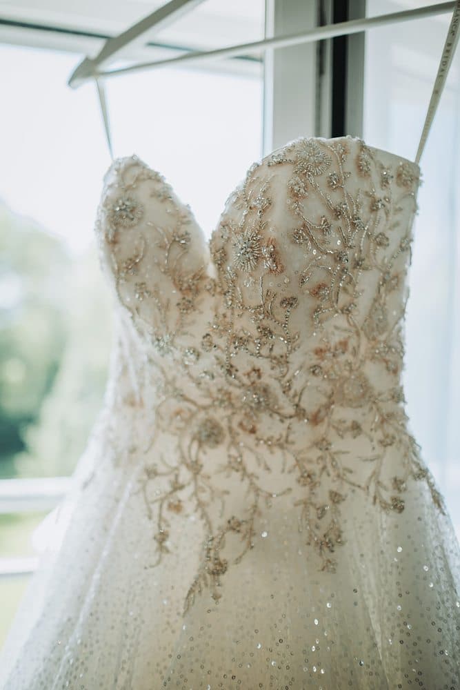 Ein Hochzeitskleid hängt auf einem Kleiderbügel vor einem Fenster.