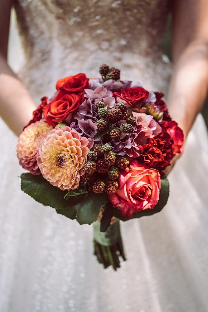Eine Braut hält einen Strauß roter und orangefarbener Blumen.