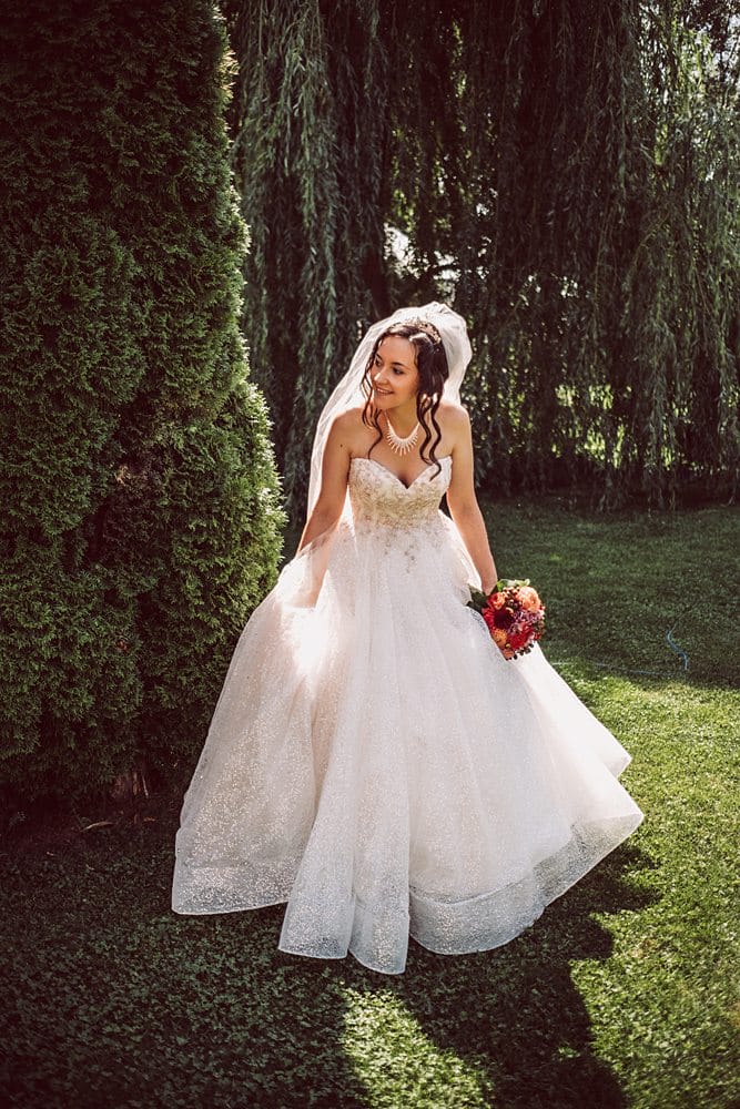 Eine Braut in einem Hochzeitskleid posiert vor einem Baum.