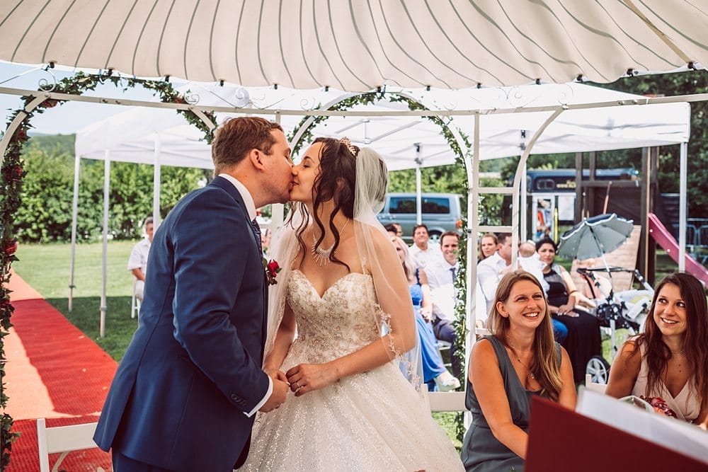 Eine Braut und ein Bräutigam küssen sich während ihrer Hochzeitszeremonie unter einem Zelt.
