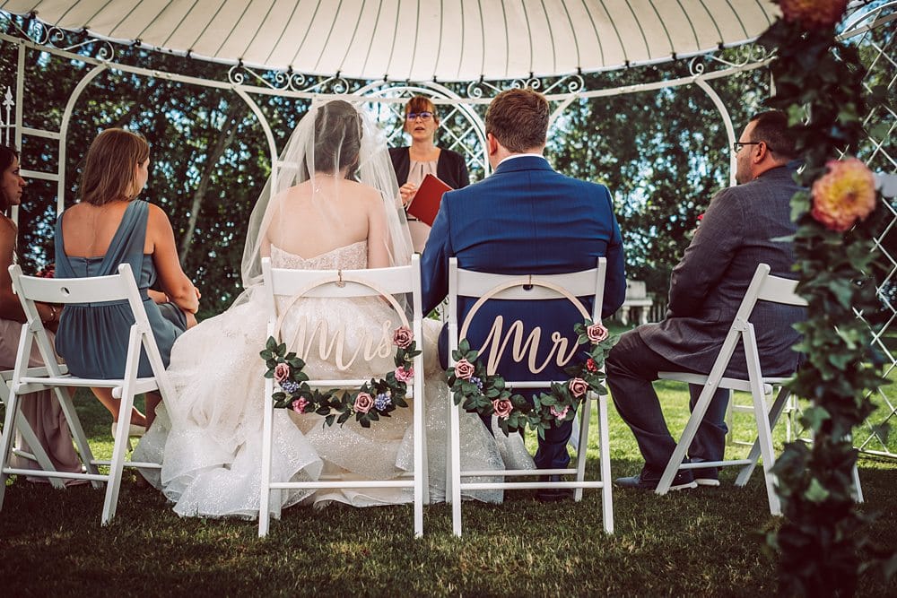 Eine Braut und ein Bräutigam sitzen auf Stühlen unter einem Pavillon.