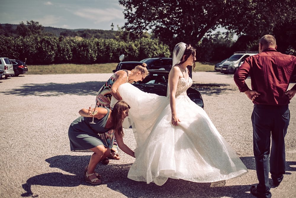 Einer Braut wird von ihren Brautjungfern in ihr Hochzeitskleid geholfen.