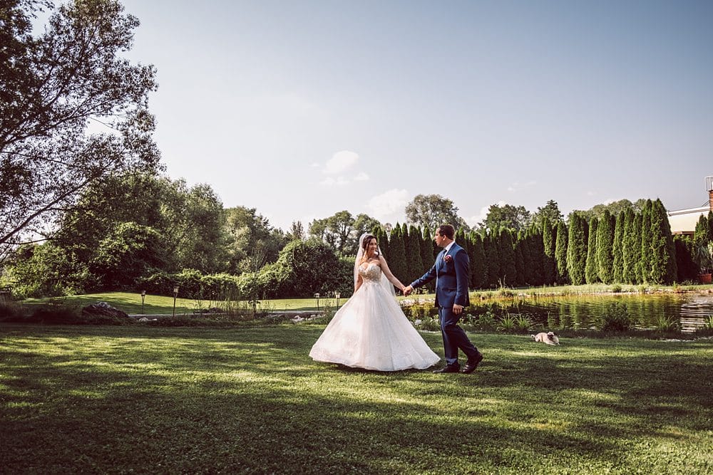 Eine Braut und ein Bräutigam gehen im Gras in der Nähe eines Teiches.