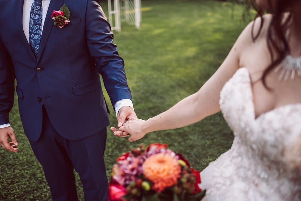 Eine Braut und ein Bräutigam halten sich im Gras an den Händen.