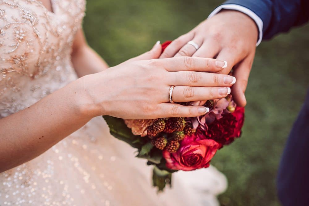 Eine Braut und ein Bräutigam halten ihre Eheringe in der Hand.