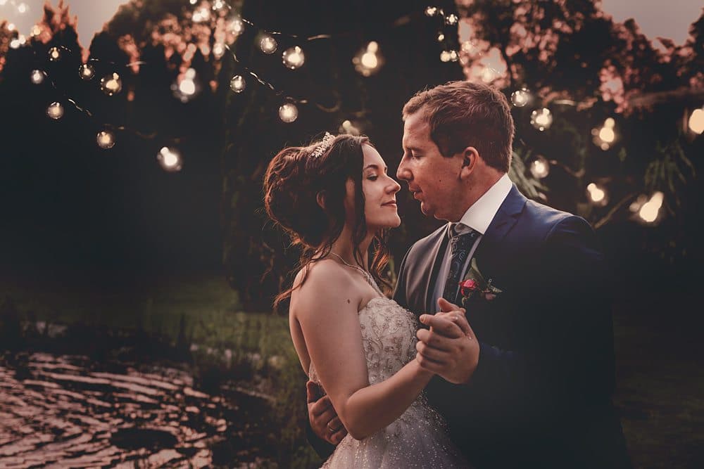 Eine Braut und ein Bräutigam stehen vor einem Teich mit Lichterketten.