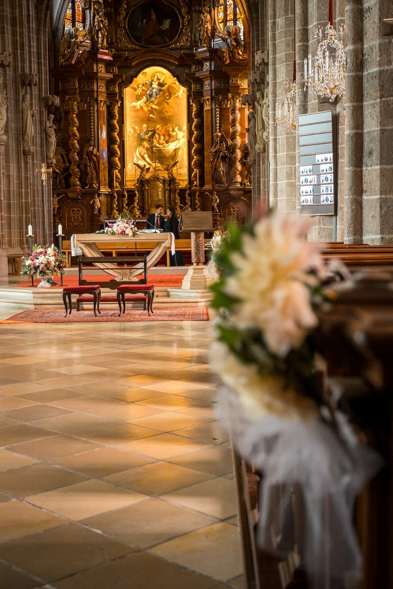 Eine Hochzeitszeremonie in einer Kirche mit Blumen auf den Kirchenbänken.