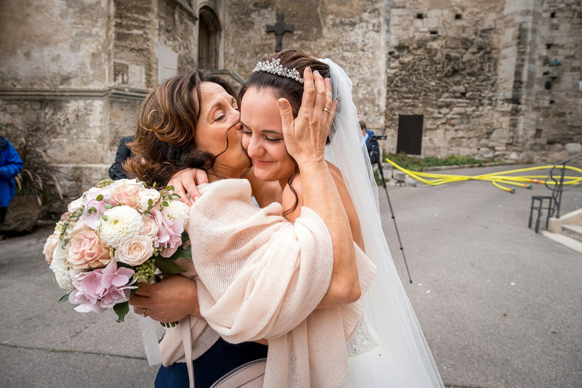 Eine Braut umarmt ihre Mutter vor einem Schloss.