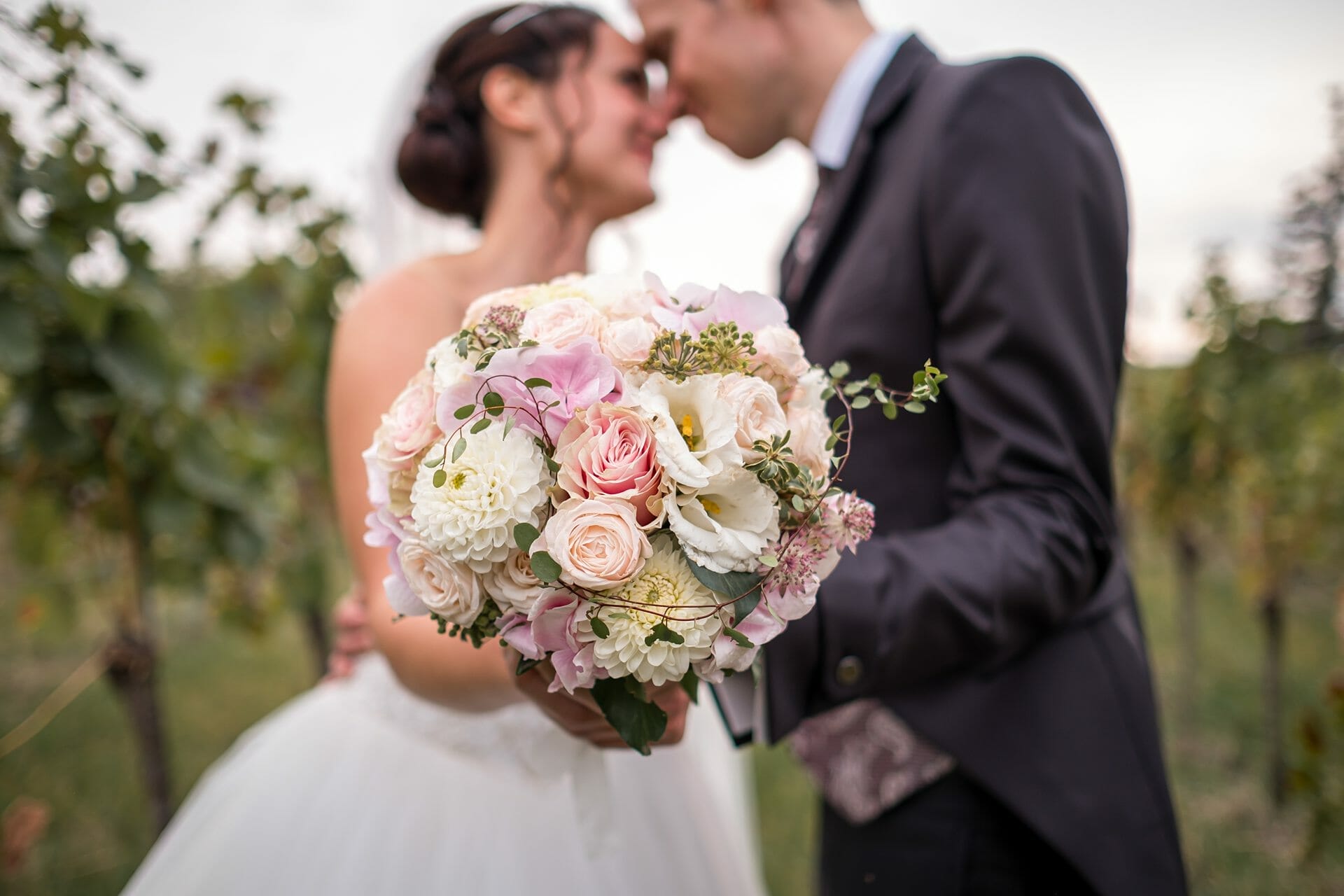 Ein Brautpaar küsst sich vor einem Weinberg.