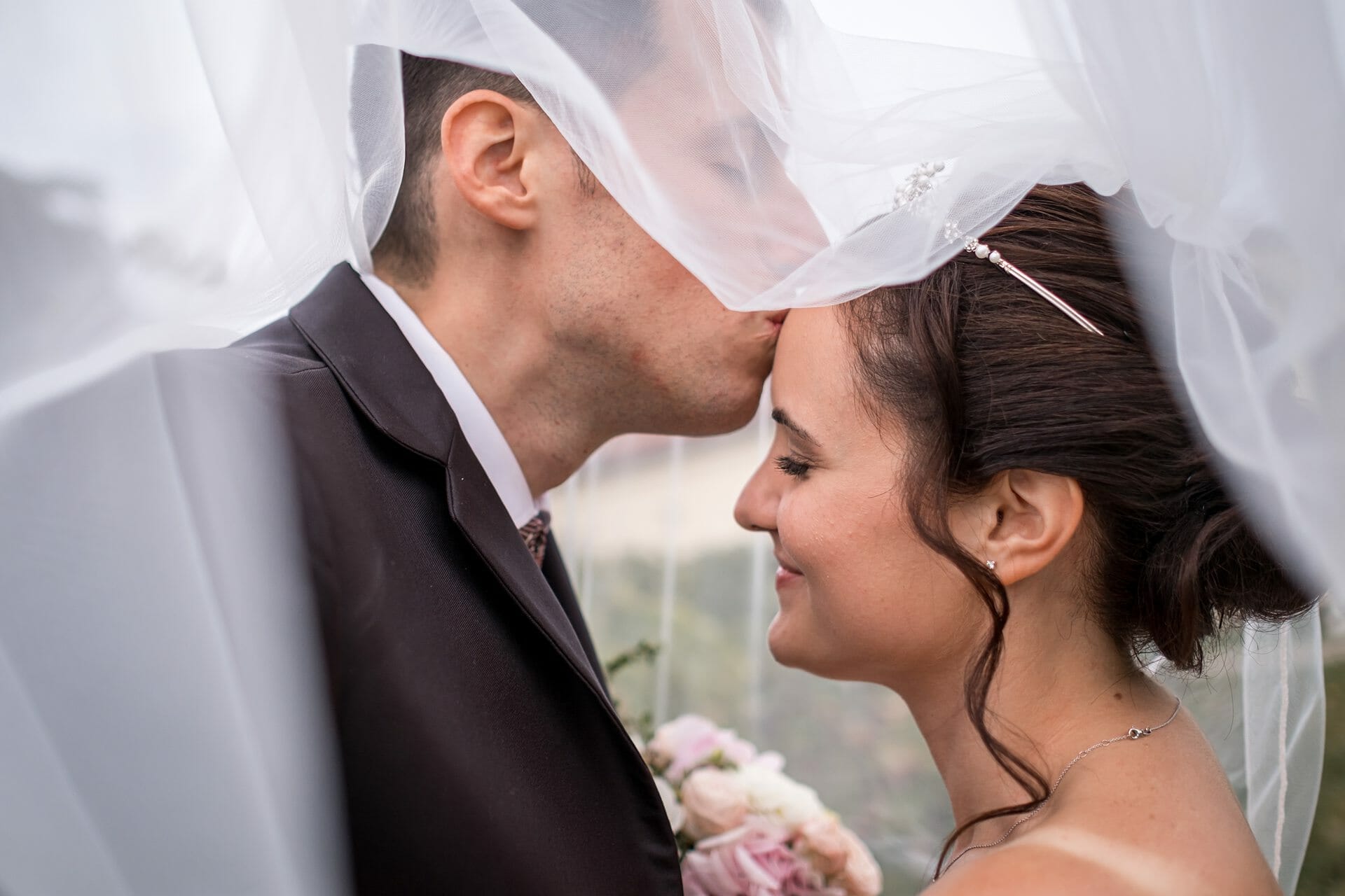 Eine Braut und ein Bräutigam küssen sich unter einem Schleier.