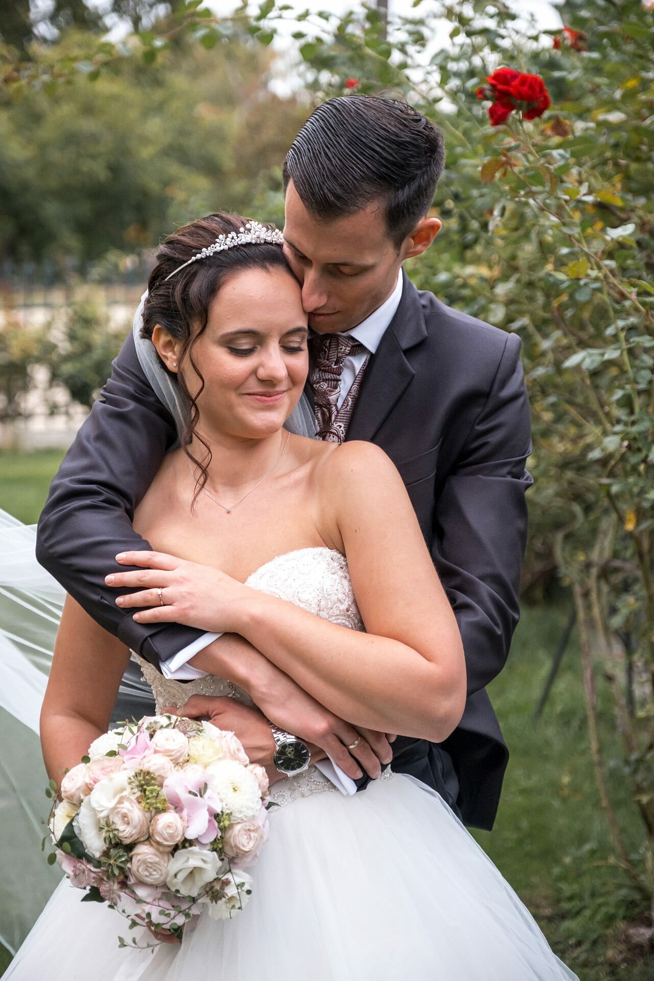 Eine Braut und ein Bräutigam umarmen sich vor einem Rosengarten.