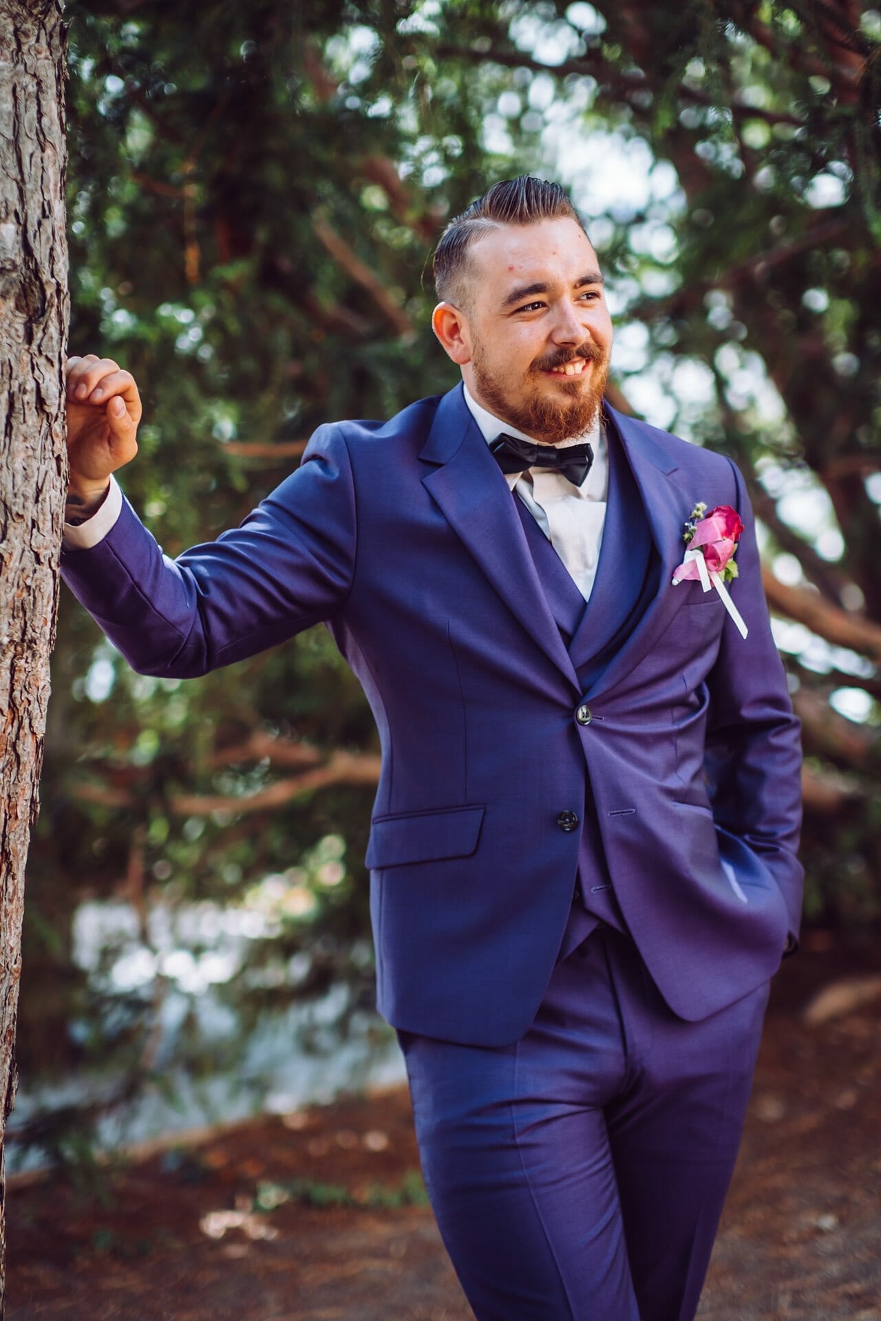 Ein Bräutigam im blauen Anzug lehnt an einem Baum.
