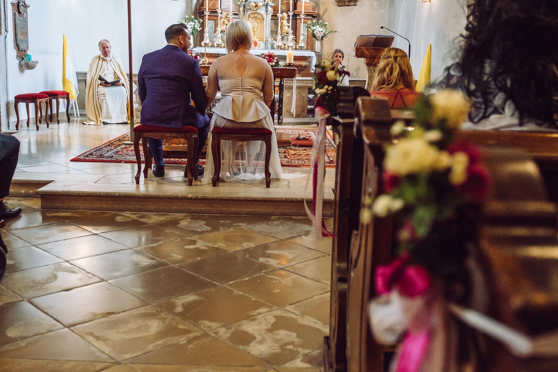 Eine Hochzeitszeremonie in einer Kirche mit einem Brautpaar, das auf den Kirchenbänken sitzt.